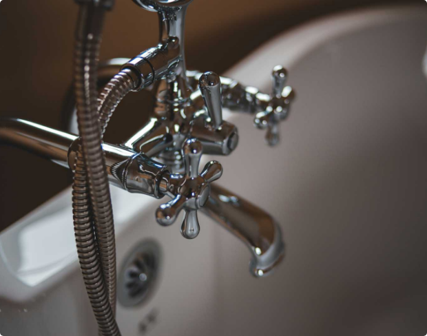 Close up of a large chrome tap at the end of a white bath tub.